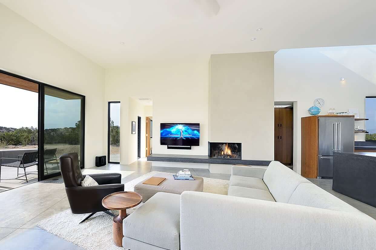 A Santa Fe-inspired living room with large windows and a fireplace, designed and constructed by a skilled home builder.
