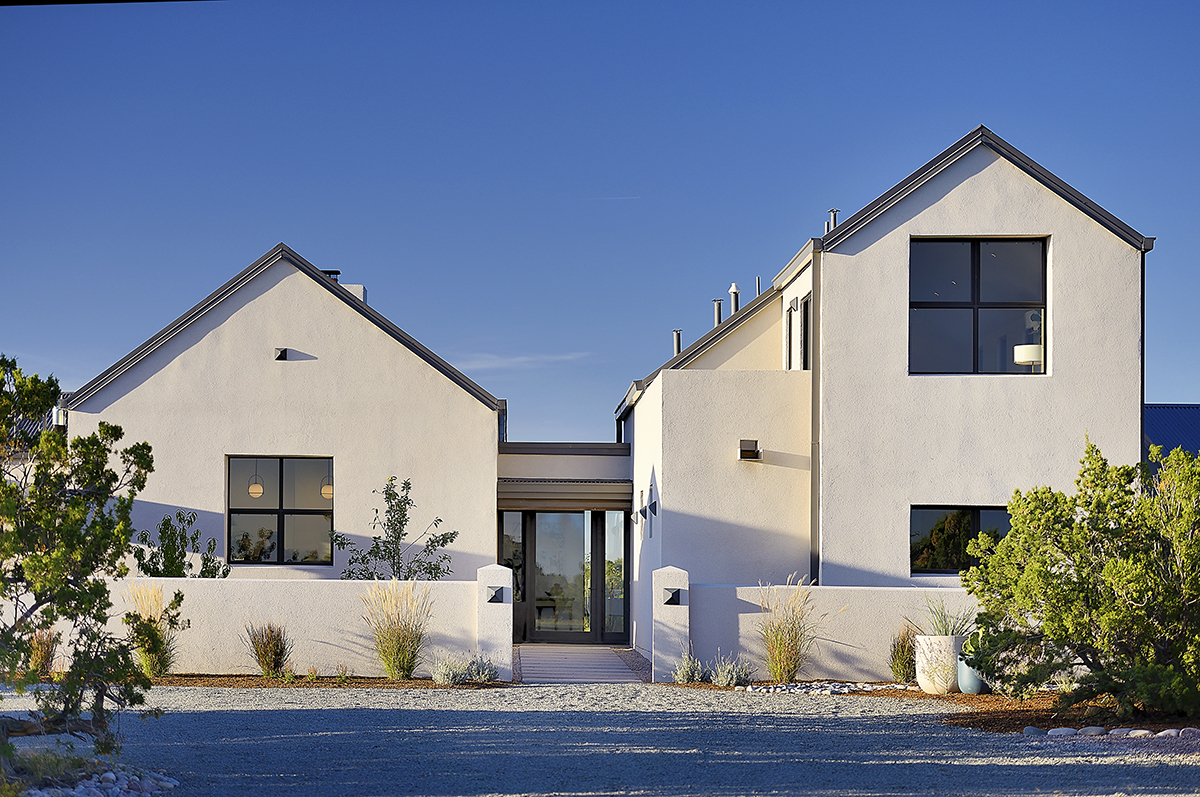 A white house with a driveway in the desert designed by an architect in Santa Fe.