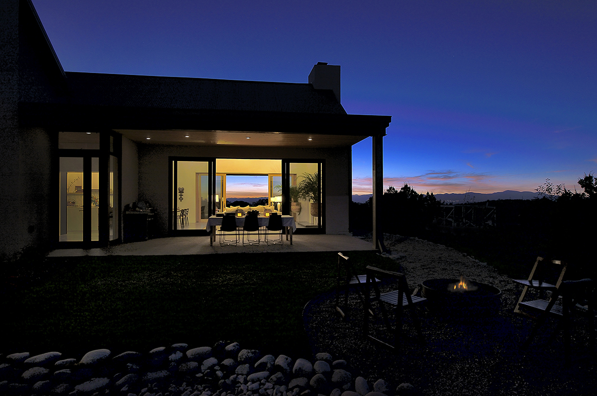 A house at dusk expertly designed by an architect, featuring a cozy fire pit in the yard.