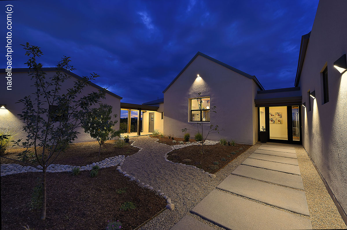 A Santa Fe inspired pathway leading to a house at night, designed by an architect.