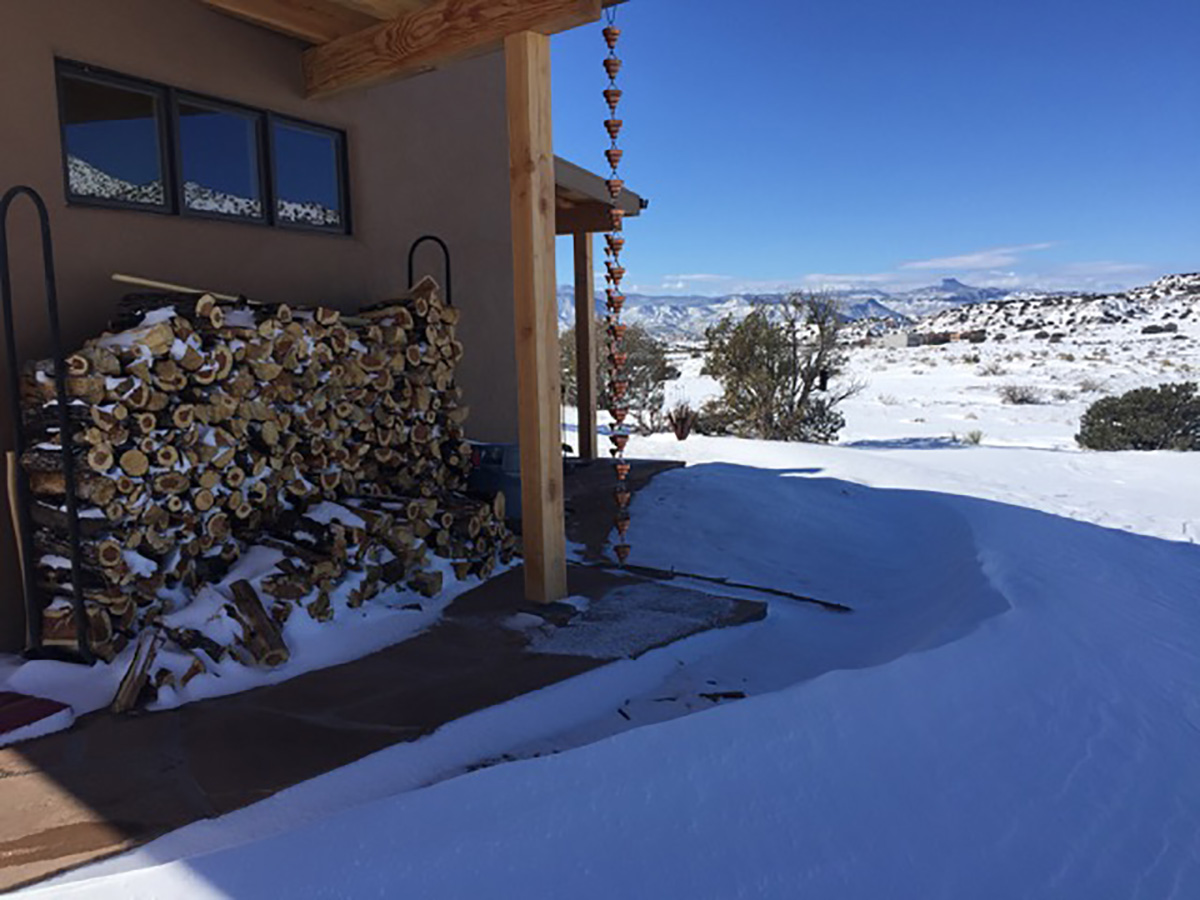 A pile of wood in front of a house in the snow, waiting to be utilized by a contractor for home renovation projects.