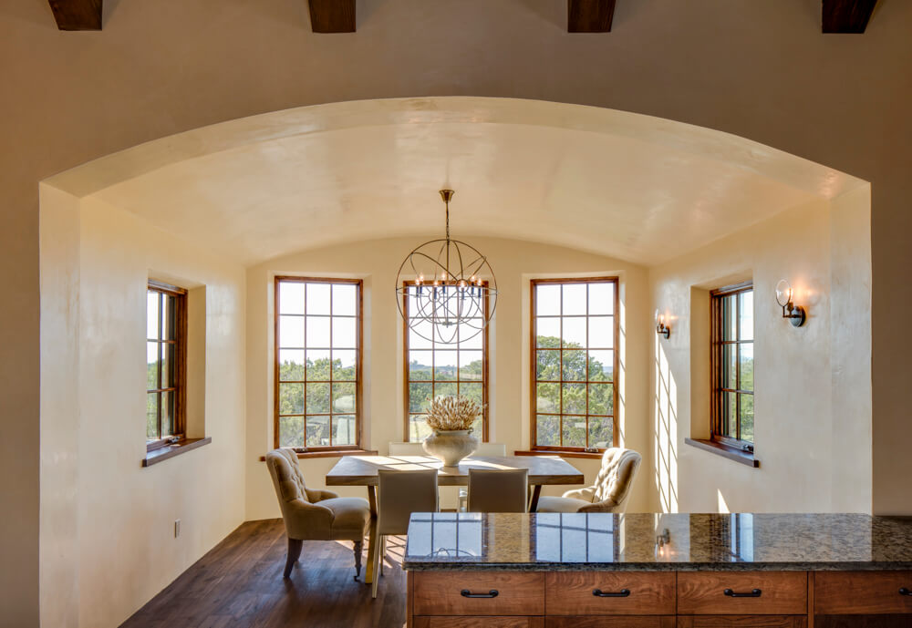 A Santa Fe-style dining room with arched windows and wooden floors built by a home builder.