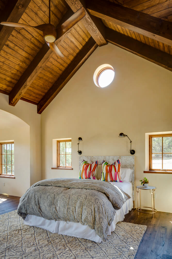 A bedroom designed by a home builder with wooden beams and a ceiling fan.
