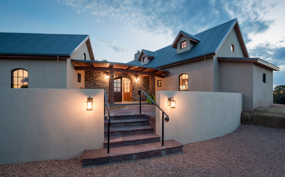 A Santa Fe home with a stone walkway and lighting at dusk, designed by a talented home designer.