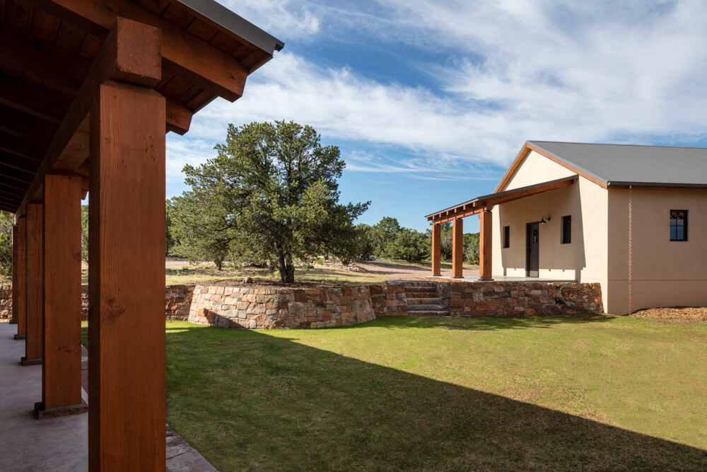 A stone house with a wooden porch and a grassy yard designed by an architect.
