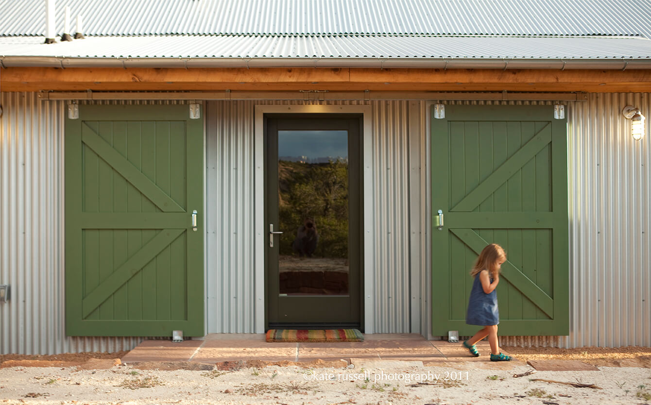A little girl standing in front of a home builder's green barn door.