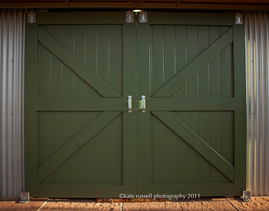 A green barn door with two metal handles designed by a home designer.