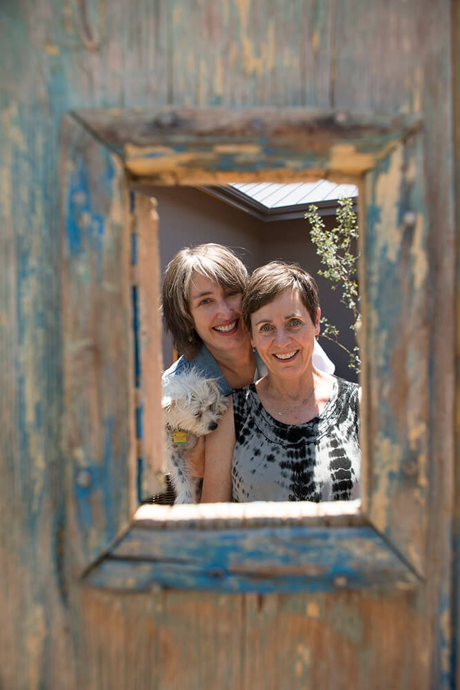 Two women, including a home designer, smiling and looking through a frame.