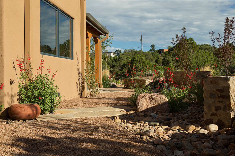 A Santa Fe style house with a stone walkway and a rock garden built by a reputable home builder and contractor.