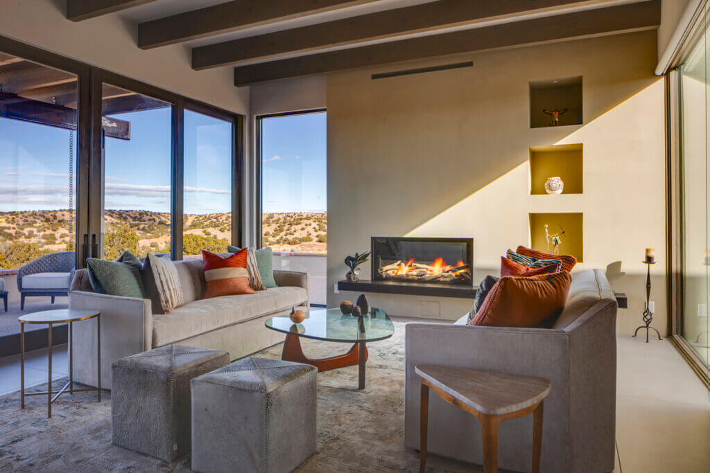 A Santa Fe style living room with large windows and a fireplace designed by a home builder or architect.
