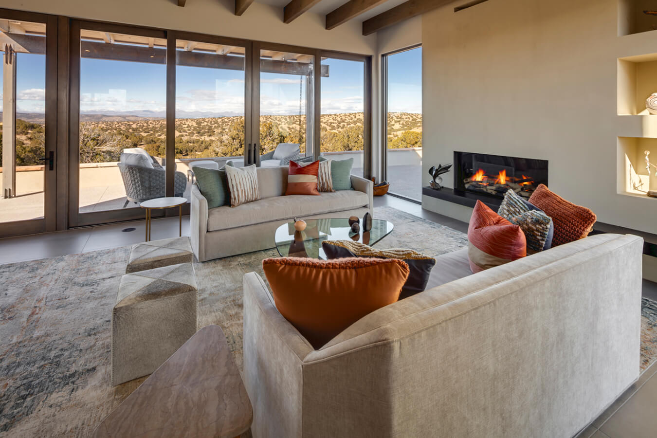 A large living room with a fireplace and a view of the mountains, designed by a Santa Fe home designer.