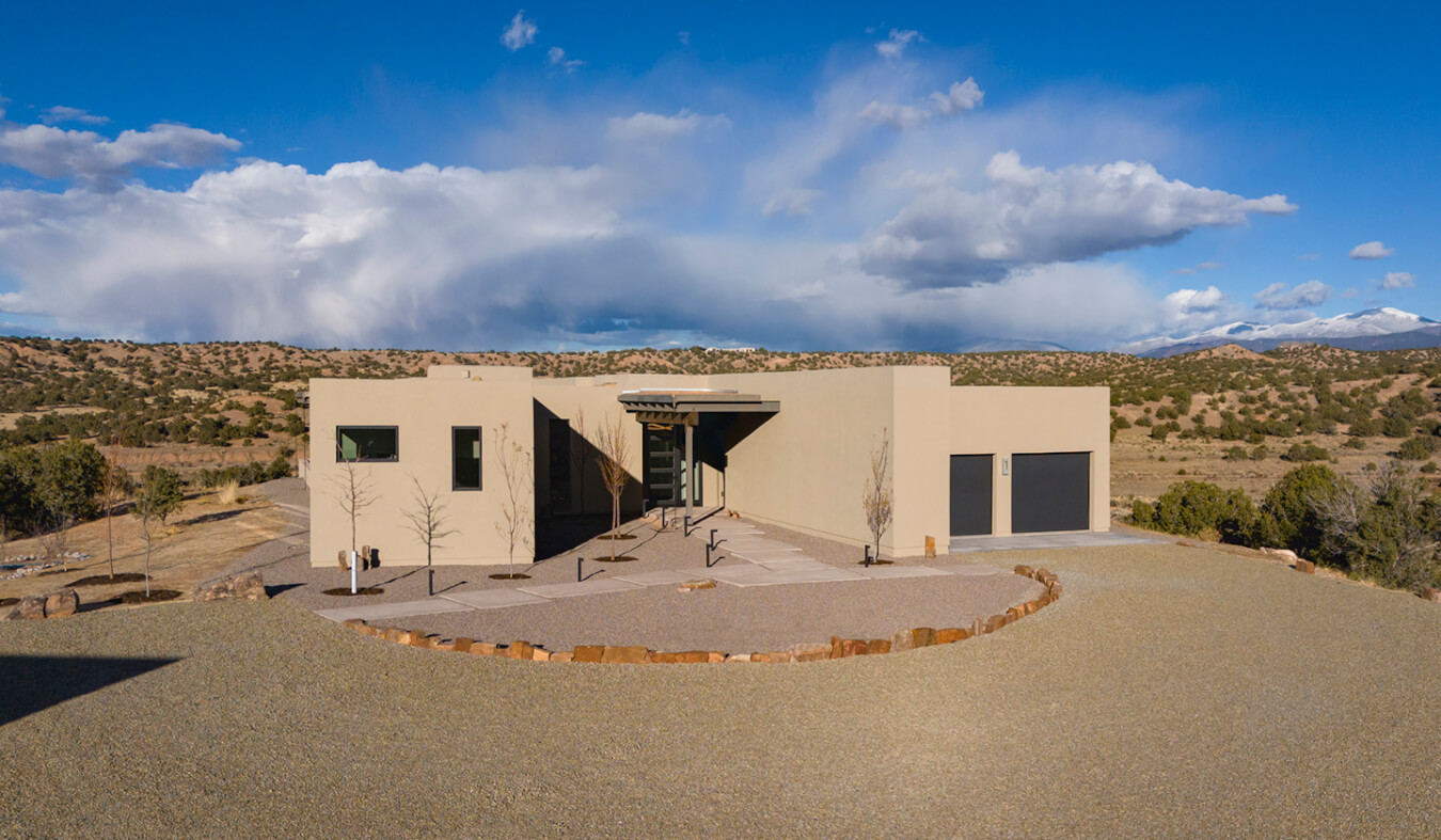 A Santa Fe style home with a driveway and a blue sky, designed by an architect.